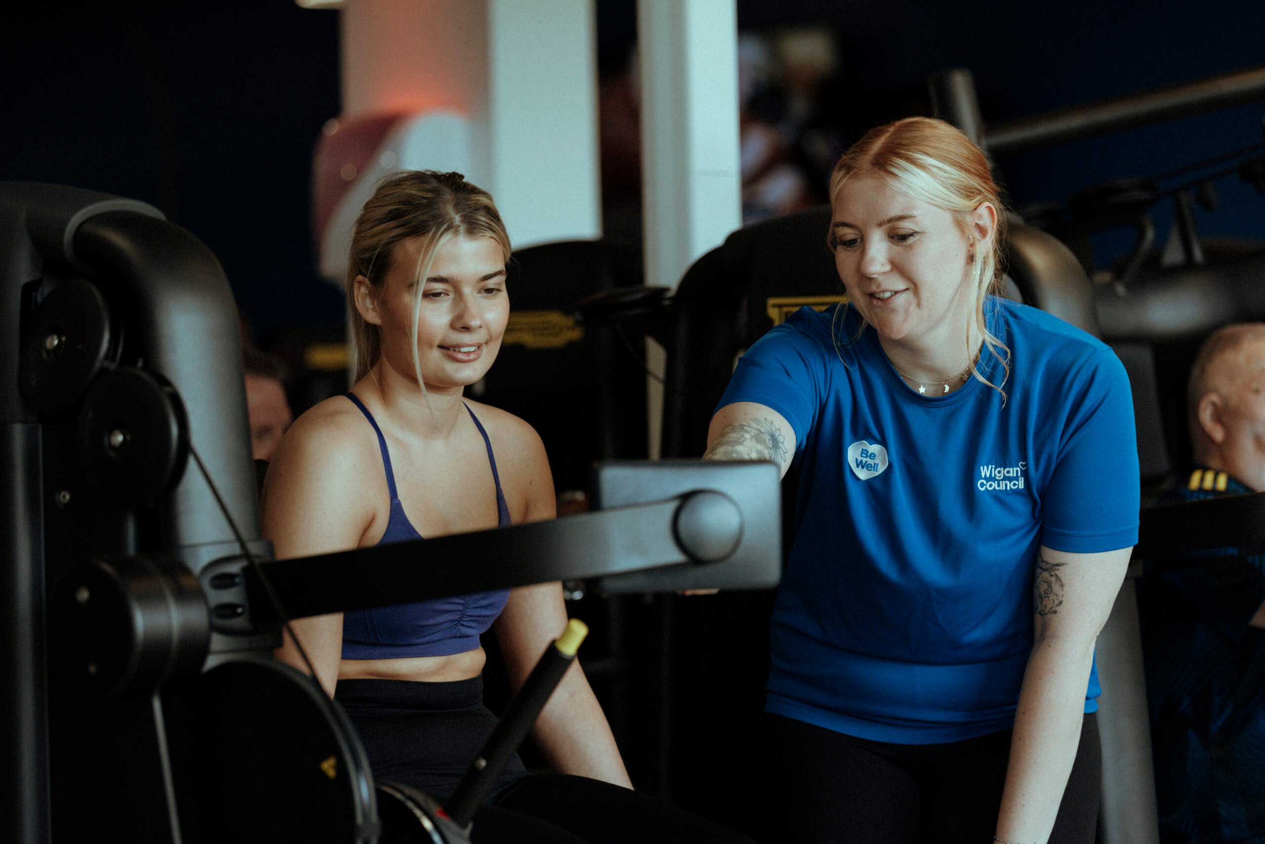 A personal trainer teaching a woman to use a machine