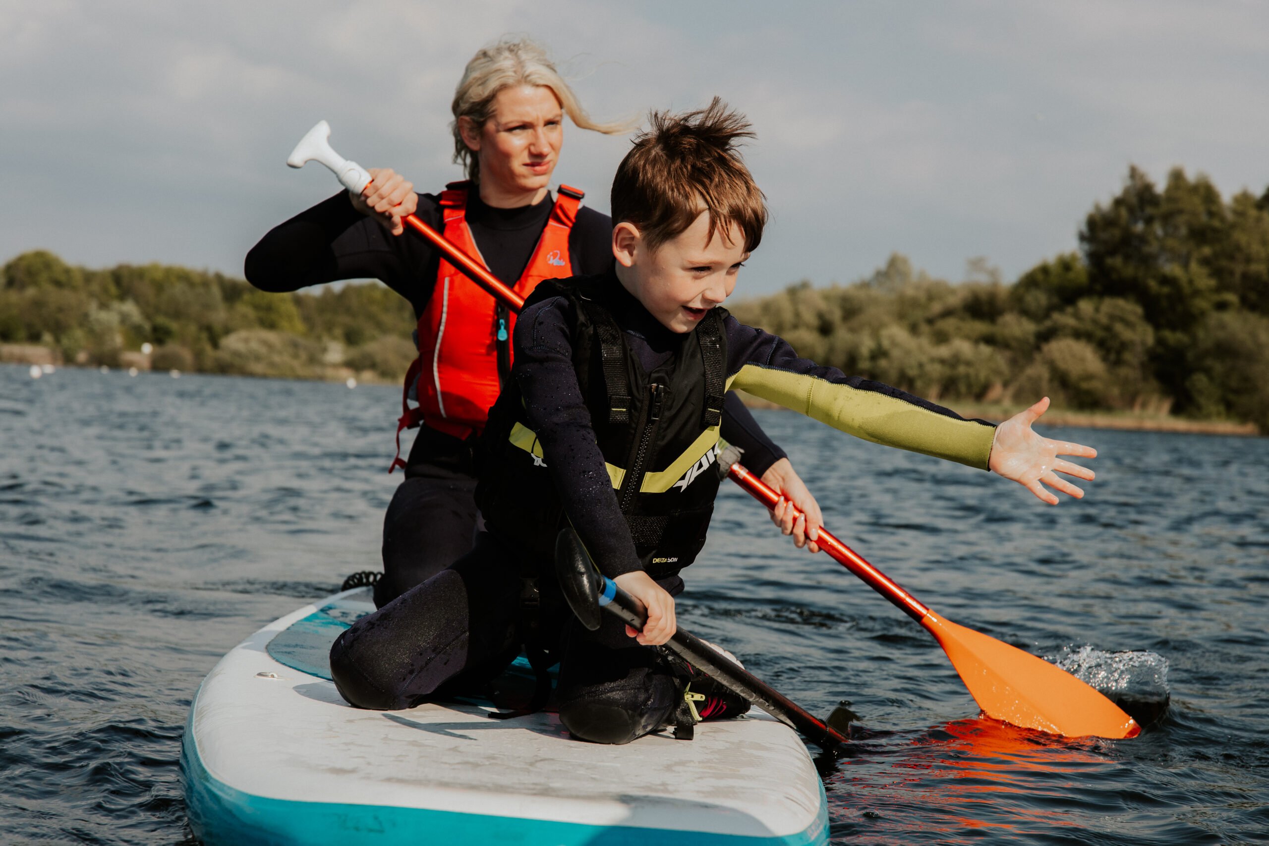 A young boy paddleboarding with his mum
