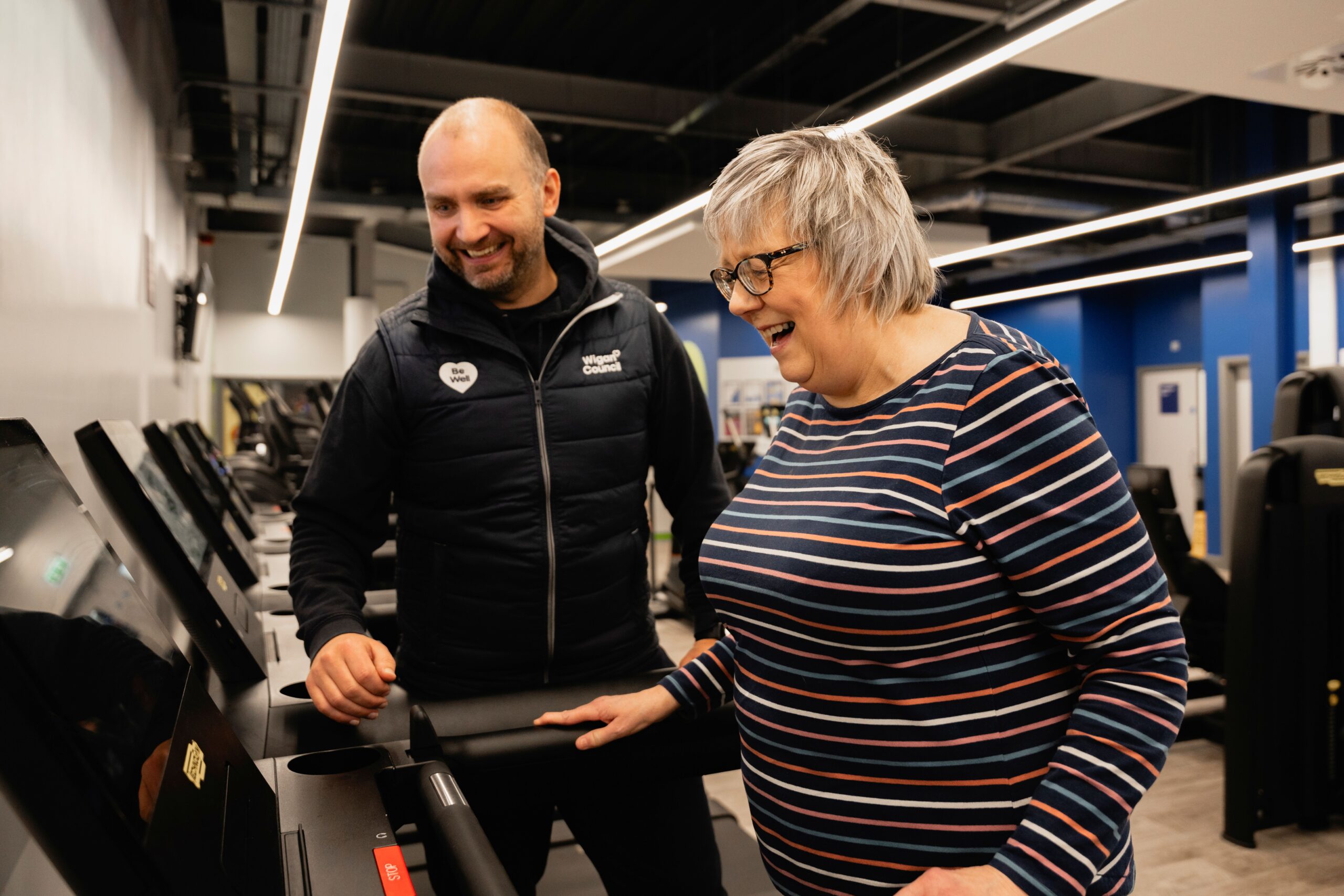 A male instructor helping a female customer on a treadmill
