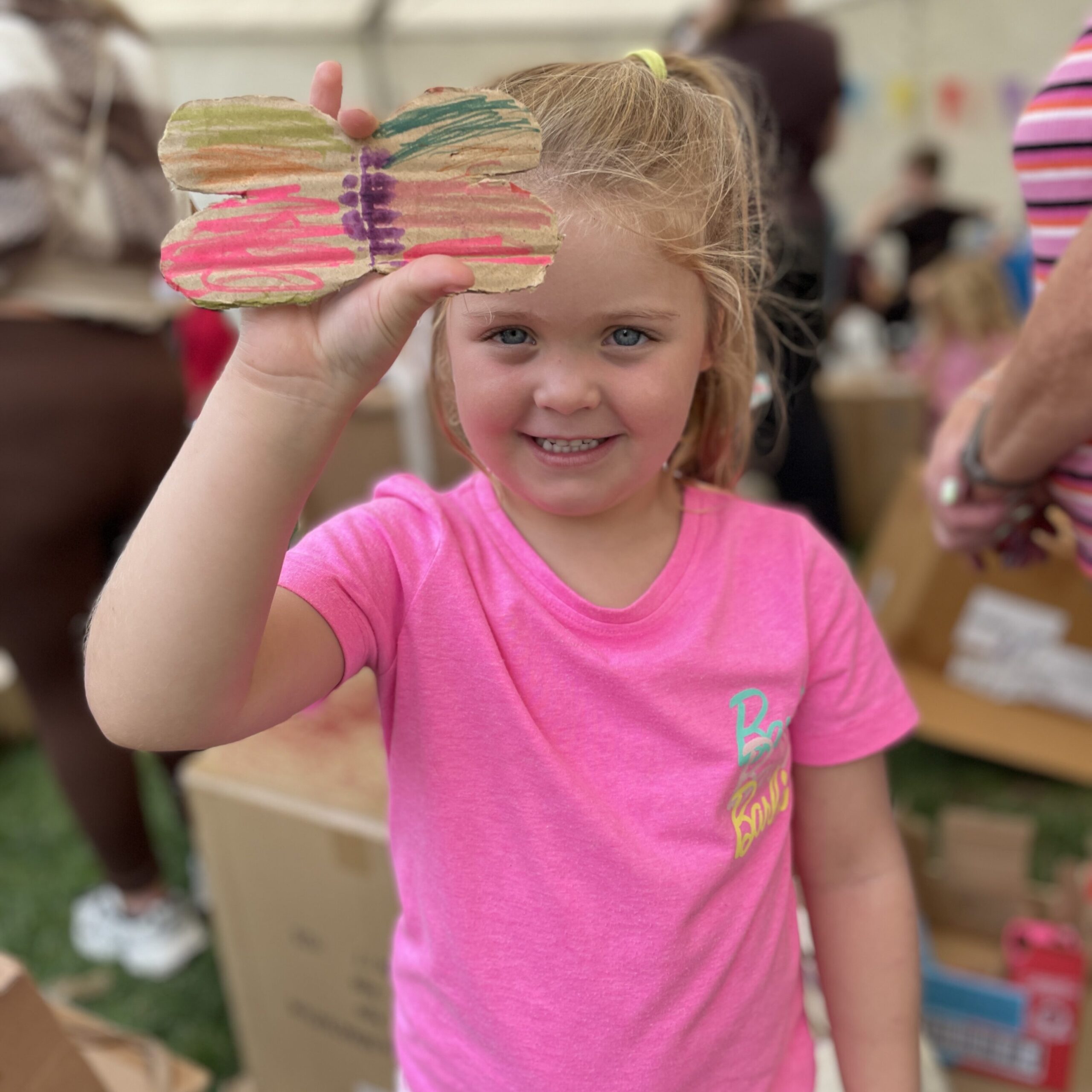 A young girl holds up a colourful cardboard butterfly